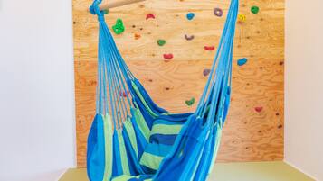 Una silla hamaca azul colgada del techo de madera, con una pared de escalada al fondo.