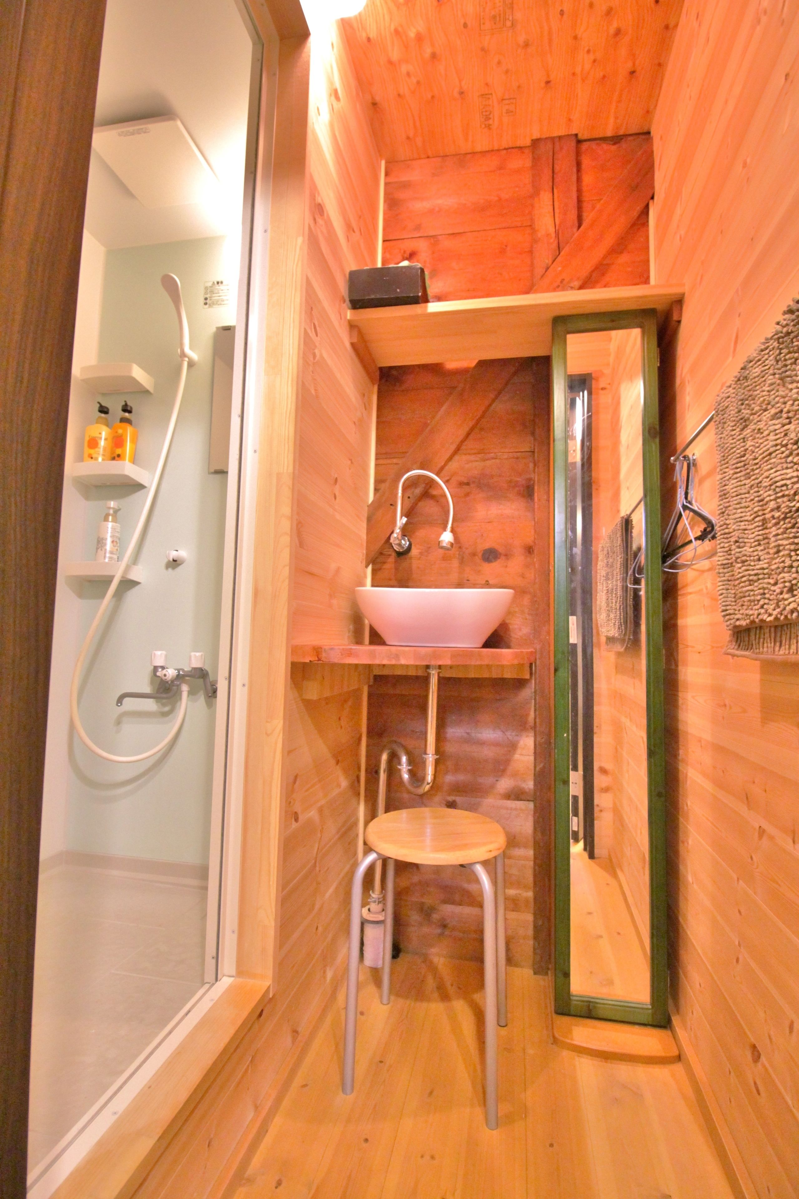 A wooden cabin bathroom with a shower, sink, and mirror.