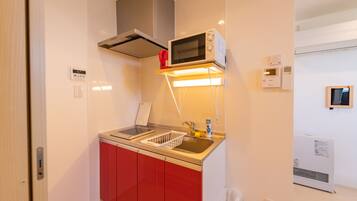 A compact kitchen with a microwave, sink, and red cabinets.