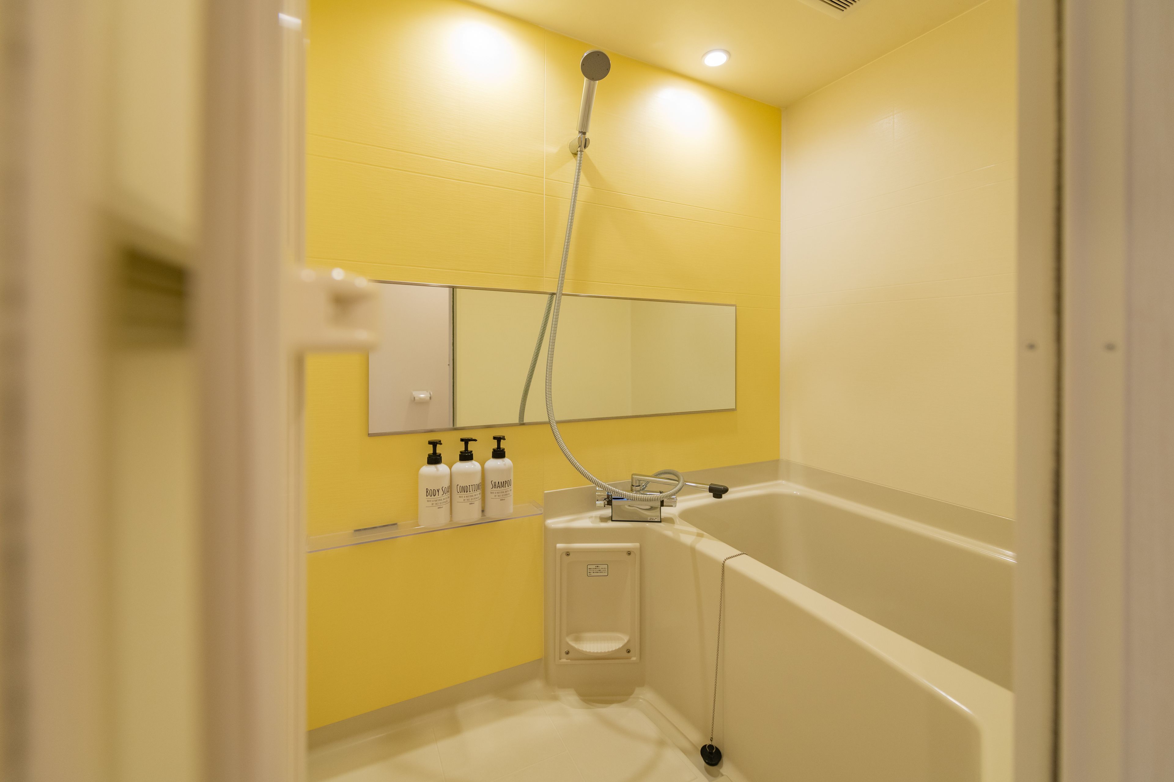 A bathroom with a yellow wall, a white bathtub, and a handheld showerhead.
