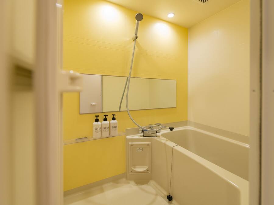 A bathroom with a yellow wall, a white bathtub, and a handheld showerhead.