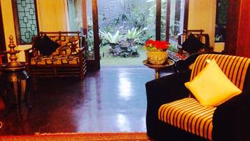 A room with a sofa, a small table with a vase of flowers, and a view of a garden.