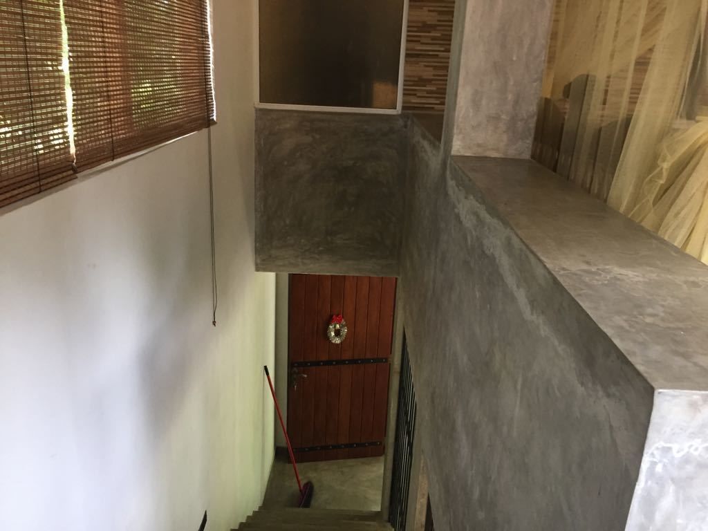 A staircase leading to a wooden door with a wreath, a window with blinds, and a textured wall.
