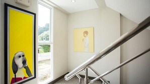 A staircase with metal railings, a yellow framed painting on the left, and a smaller painting on the right. - Central Residences (Wichit)