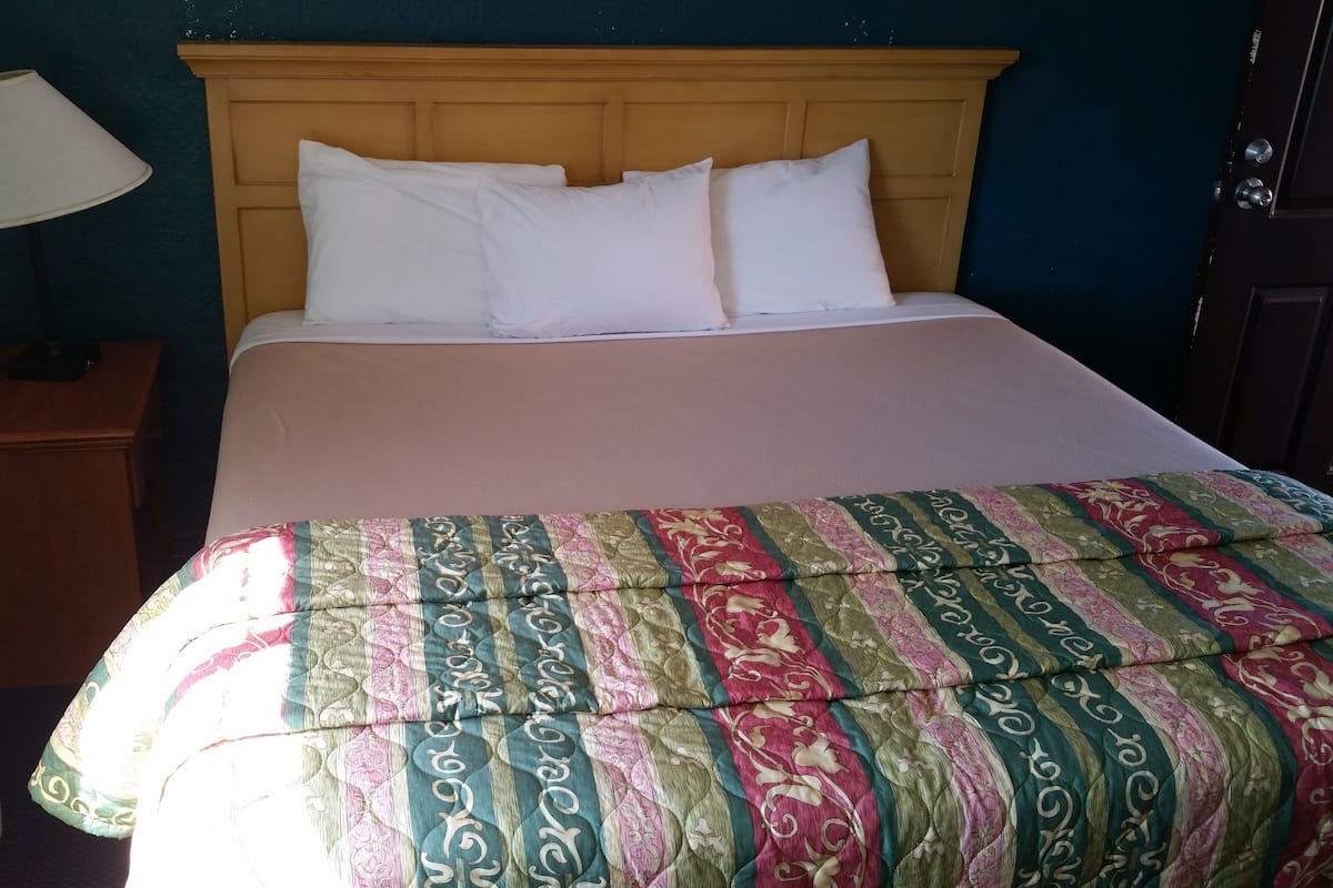 A bed with a patterned bedspread, a bedside lamp, and a heater on the floor.