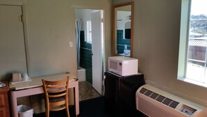 Uma cozinha compacta com micro-ondas, um pequeno frigorífico, uma cadeira de madeira e uma janela com vista para um edifício.