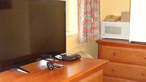 Uma cômoda de madeira com gavetas, uma TV de tela plana, um controle remoto e um micro-ondas em cima.
