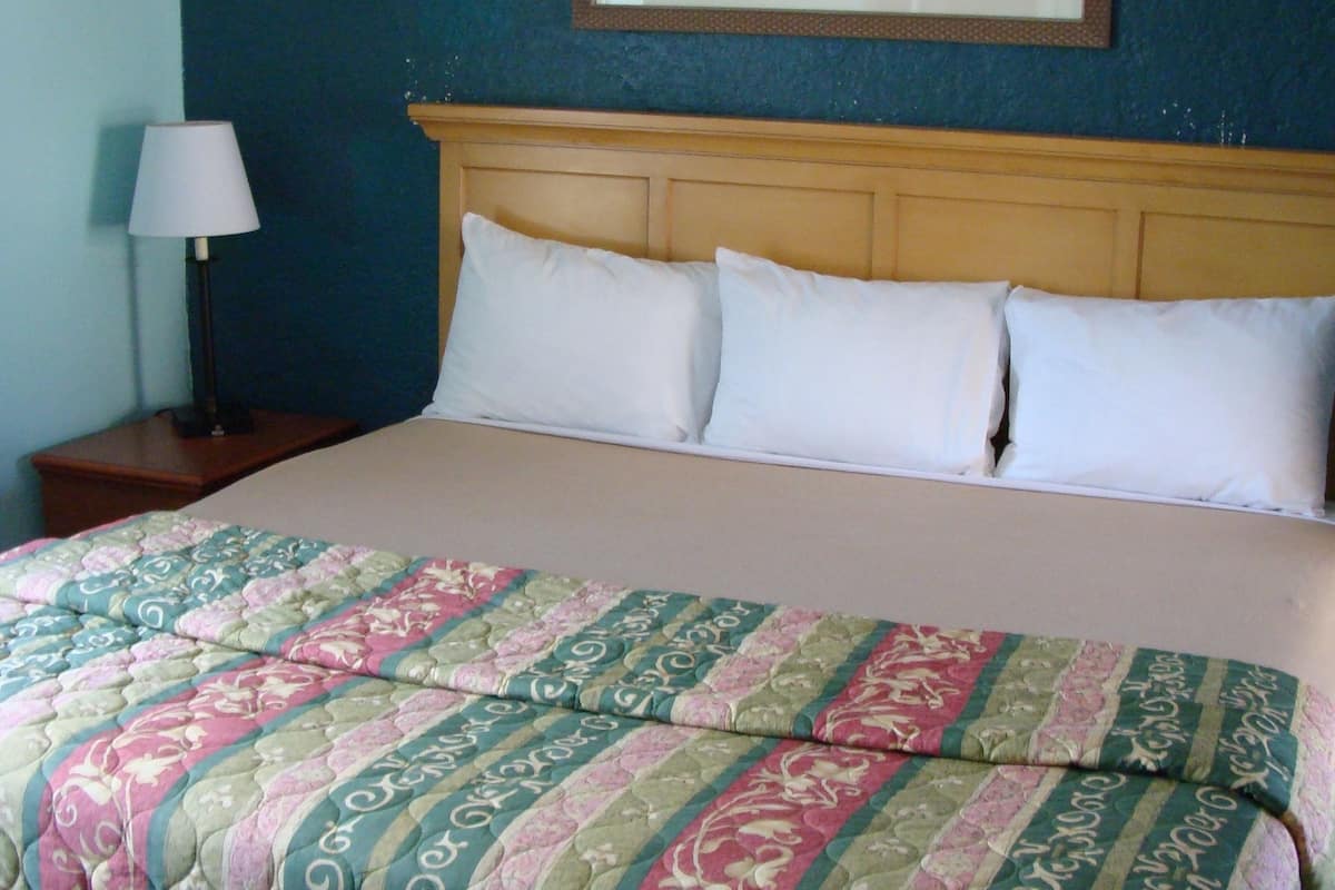 A neatly made bed with a patterned quilt, a wooden headboard, and a framed picture on the wall.