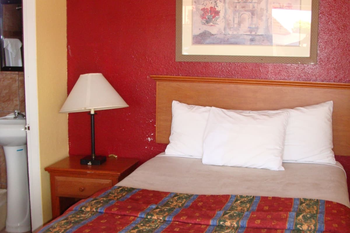 A hotel room with a bed, a nightstand, a lamp, and a framed picture on the wall.