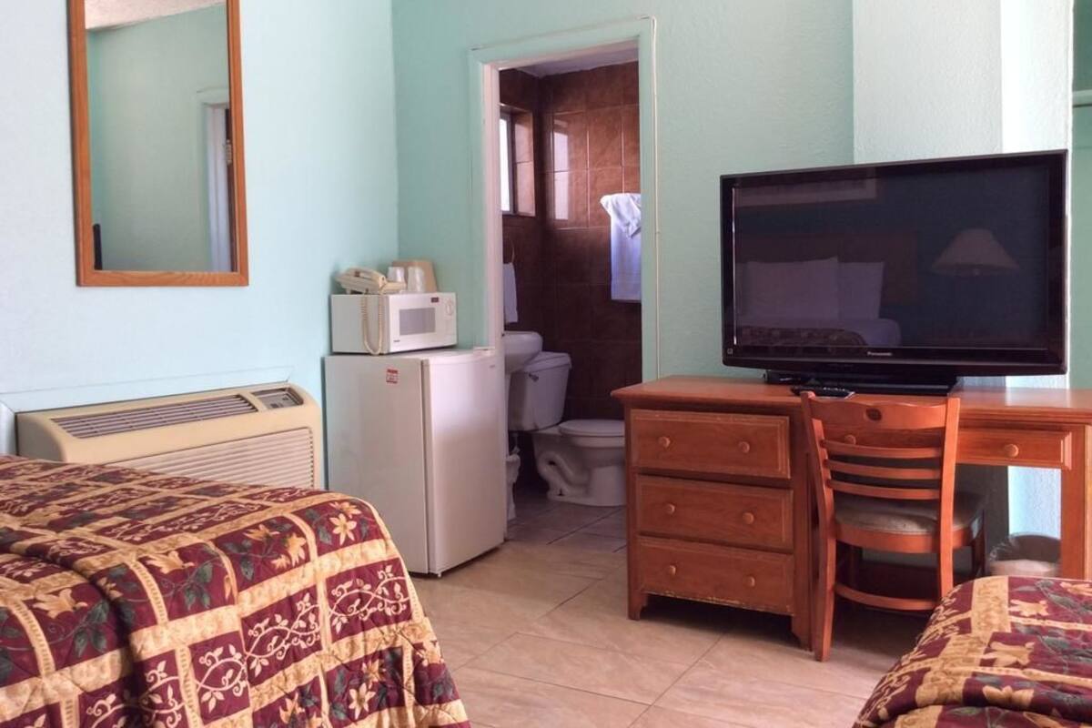 A hotel room with a bed, a TV, a dresser, a microwave, and a refrigerator.
