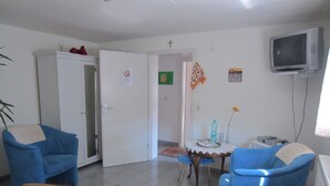 A room with a bed, two blue armchairs, a small table with a water bottle, a TV on the wall, and a door with a no-smoking sign. - Between Breisach and Staufen (Bad Krozingen)