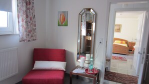 A small, red sofa in a room with a mirror, a small table with a tray, and a door leading to another room. - Between Breisach and Staufen (Bad Krozingen)