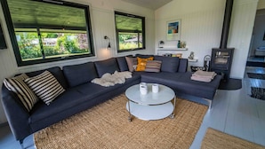 A modern living room with a dark grey sectional sofa, a round white coffee table, and a woven rug. - Cottage 150 m from Beach (Stege)