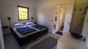 A bedroom with two beds, a window, a desk, and a door leading to a bathroom. - Cottage 150 m from Beach (Stege)