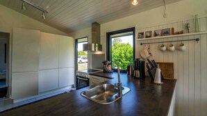 A modern kitchen with a stainless steel sink, white cabinets, and a window overlooking greenery. - Cottage 150 m from Beach (Stege)