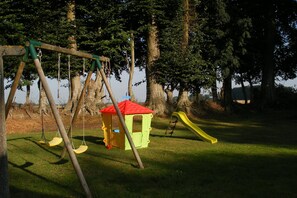 Ein Spielplatz mit Schaukeln, einer Rutsche und einem kleinen Spielhäuschen.
