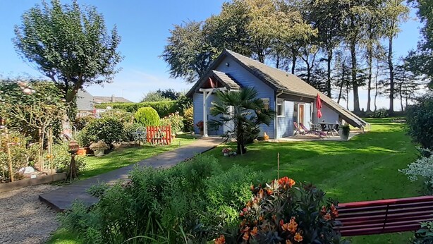Une maison avec un toit en pente, entourée d’un jardin bien entretenu où poussent différentes plantes et fleurs.