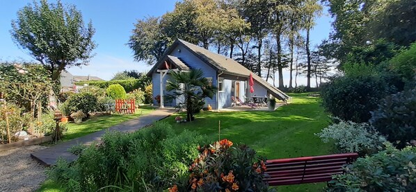 Ein Haus mit geneigtem Dach, umgeben von einem gepflegten Garten mit verschiedenen Pflanzen und Blumen.