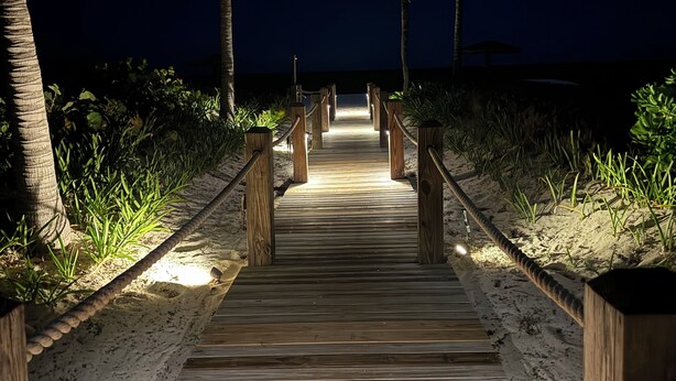 A wooden pathway leading to a beach at night, flanked by palm trees and illuminated by overhead lights. - 1 br 1ba Ocean Front Condo with amazing Sunrises (Providenciales)