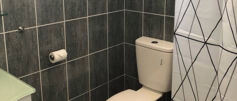 A bathroom with dark tiles, a white toilet, a green sink, and a yellow trash bin.