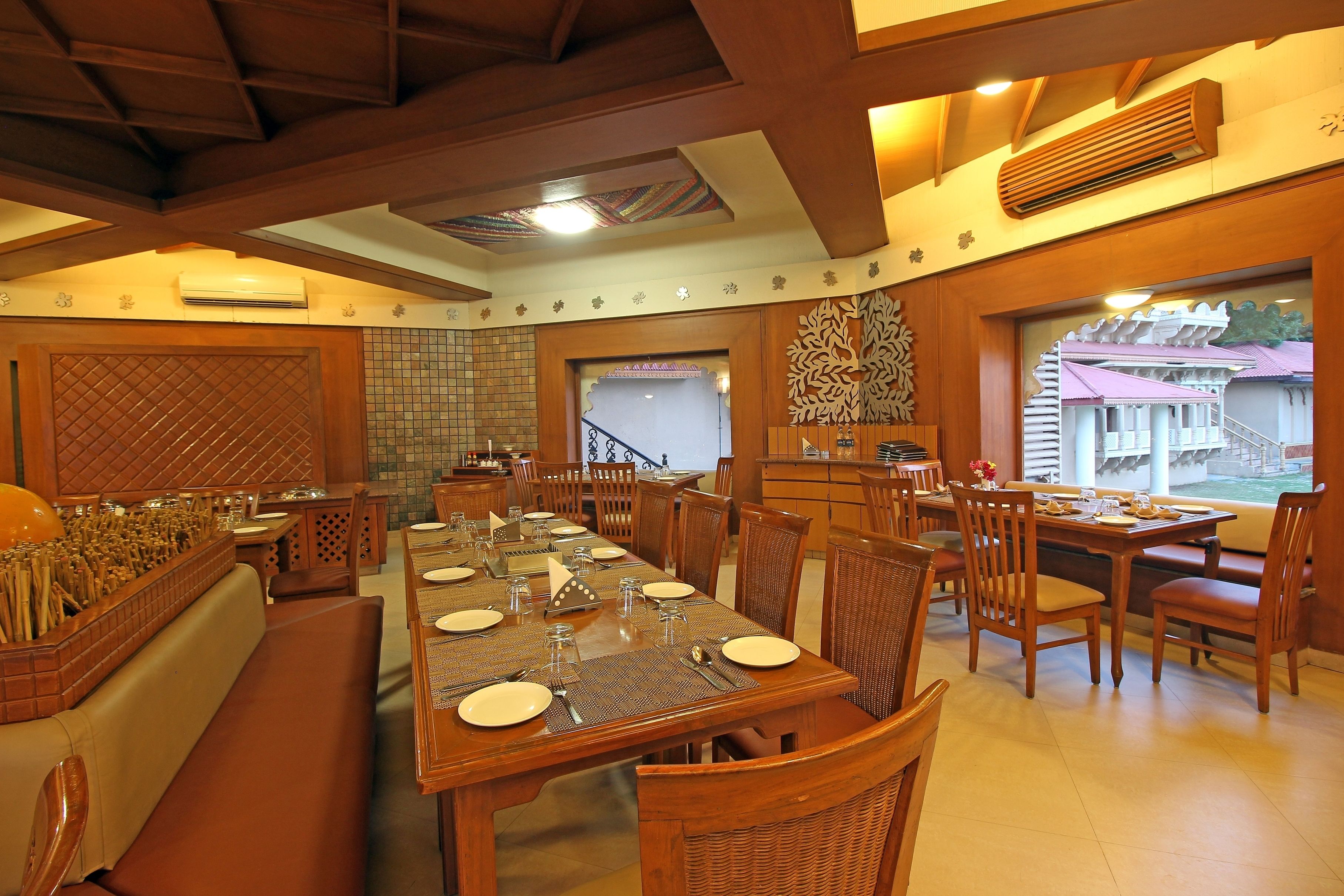 A dining area with wooden tables and chairs, a large window with a view, and a decorative wall pattern.