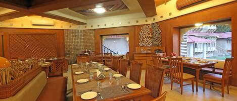 A dining area with wooden tables and chairs, a large window with a view, and a decorative wall pattern.
