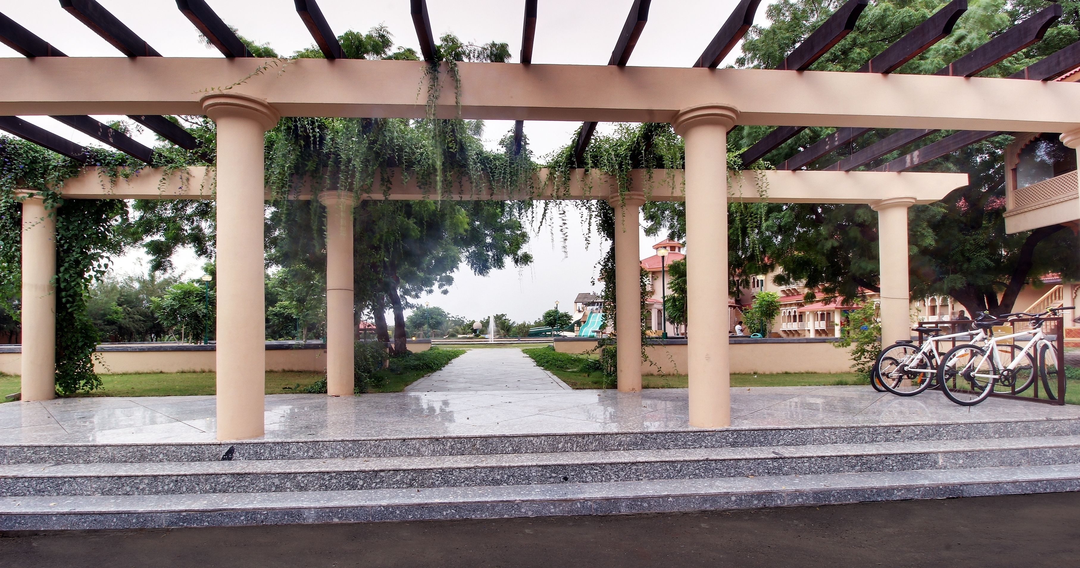 A covered outdoor area with a pergola, steps leading to a fountain, and bicycles parked nearby.