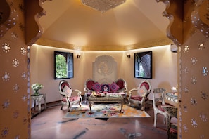 A traditional room with ornate decor, including a sofa set, patterned rugs, and wall-mounted lamps. - Gateway Kandla Gandhidham (Anjar)