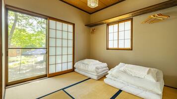 A traditional Japanese room with tatami flooring, a sliding door, and a view of greenery outside.
