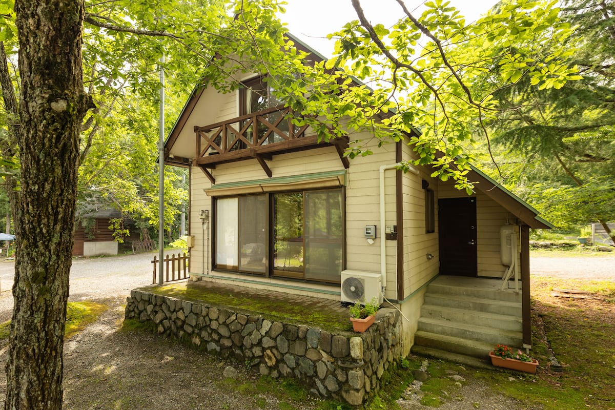 Ett litet hus i en våning med en grund av sten, stora fönster och en veranda med en krukväxt.