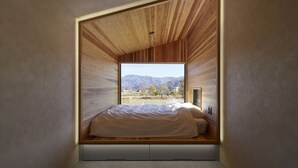 Een slaapkamer met een houten plafond en een groot raam met uitzicht op een bergachtig landschap.