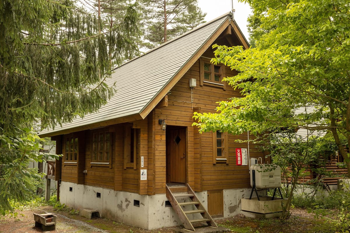 En stuga av trä med ett sluttande tak, en ytterdörr och en liten veranda.