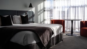Une chambre d’hôtel moderne avec un grand lit, une table ronde et une vue dégagée à travers des rideaux légers.