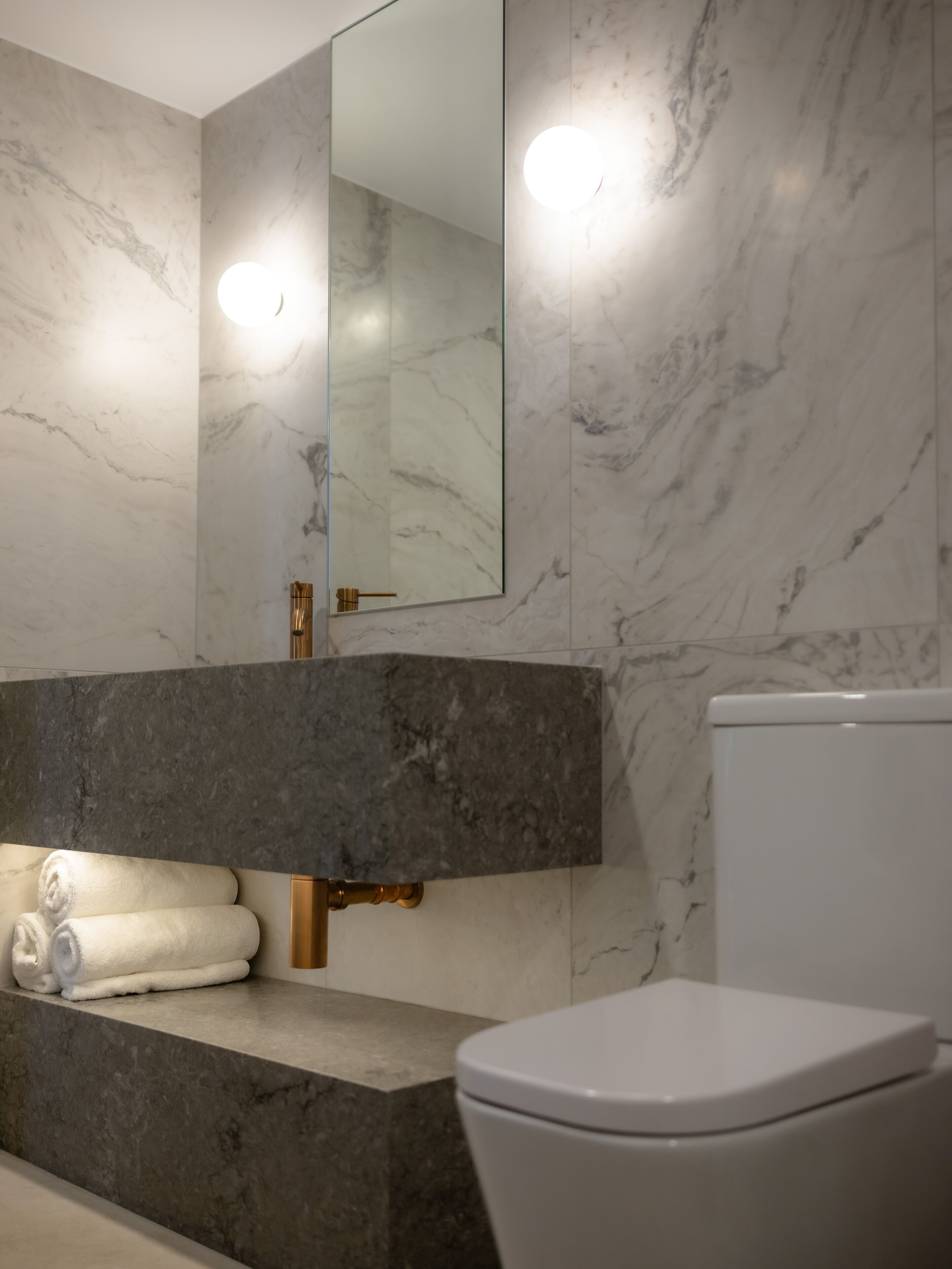 A bathroom with marble walls, a large mirror, a white toilet, and a towel rack with towels.