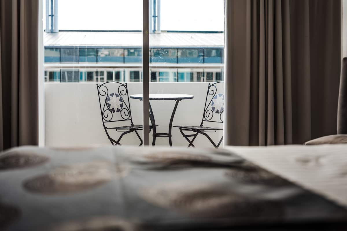 A hotel room with a balcony, a bed, and a view of the building across the street.