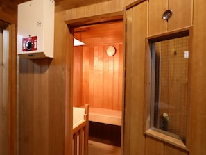 A wooden sauna room with a bench, a wall-mounted heater, and a clock. - Campagne Hakuba (Hakuba)