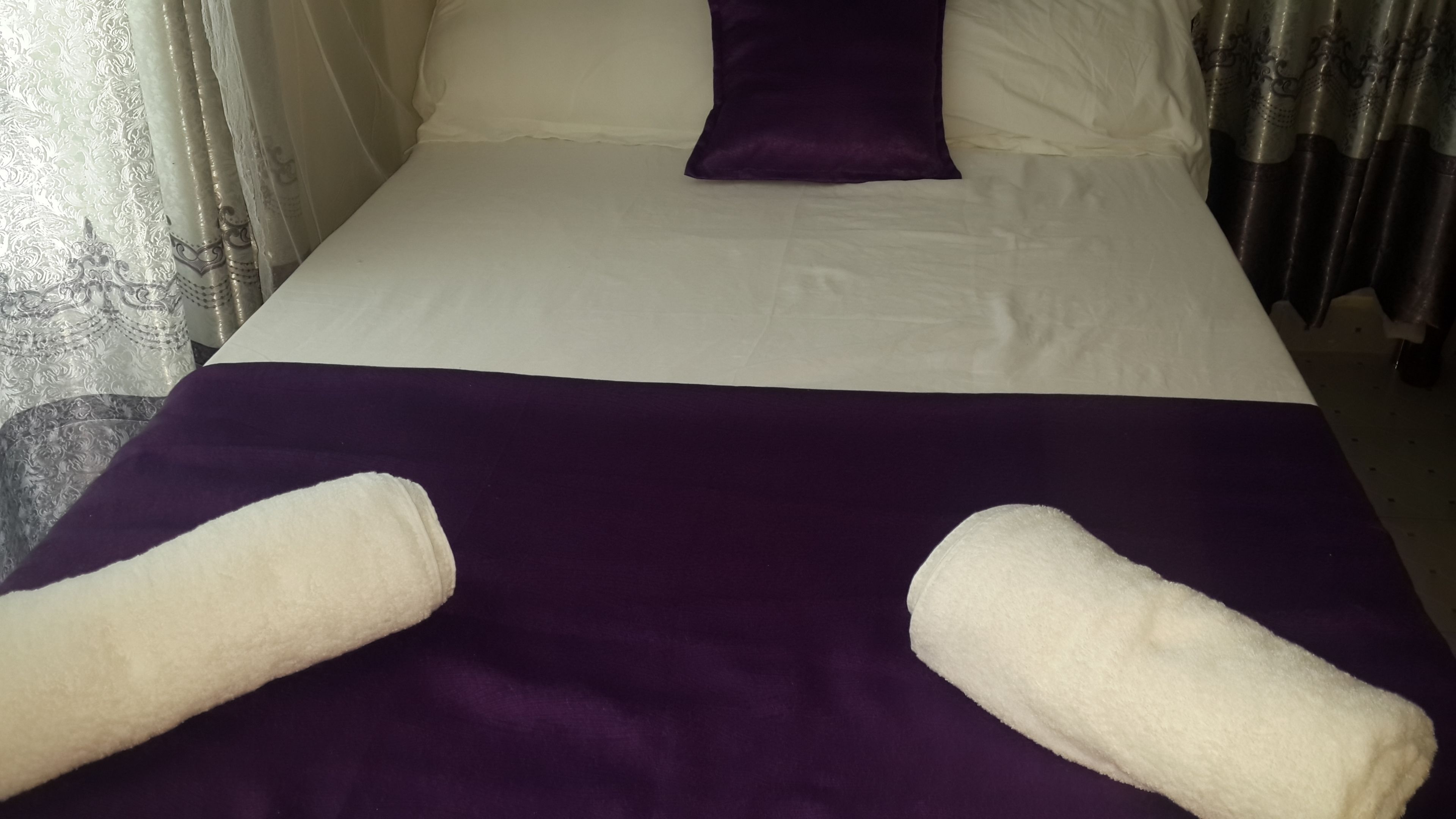A bed with a white and purple bedspread, two white towels, and a purple pillow.