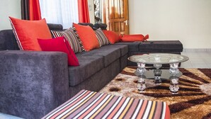 A modern living room with a grey sectional sofa, red and striped cushions, a round coffee table, and a patterned rug.
