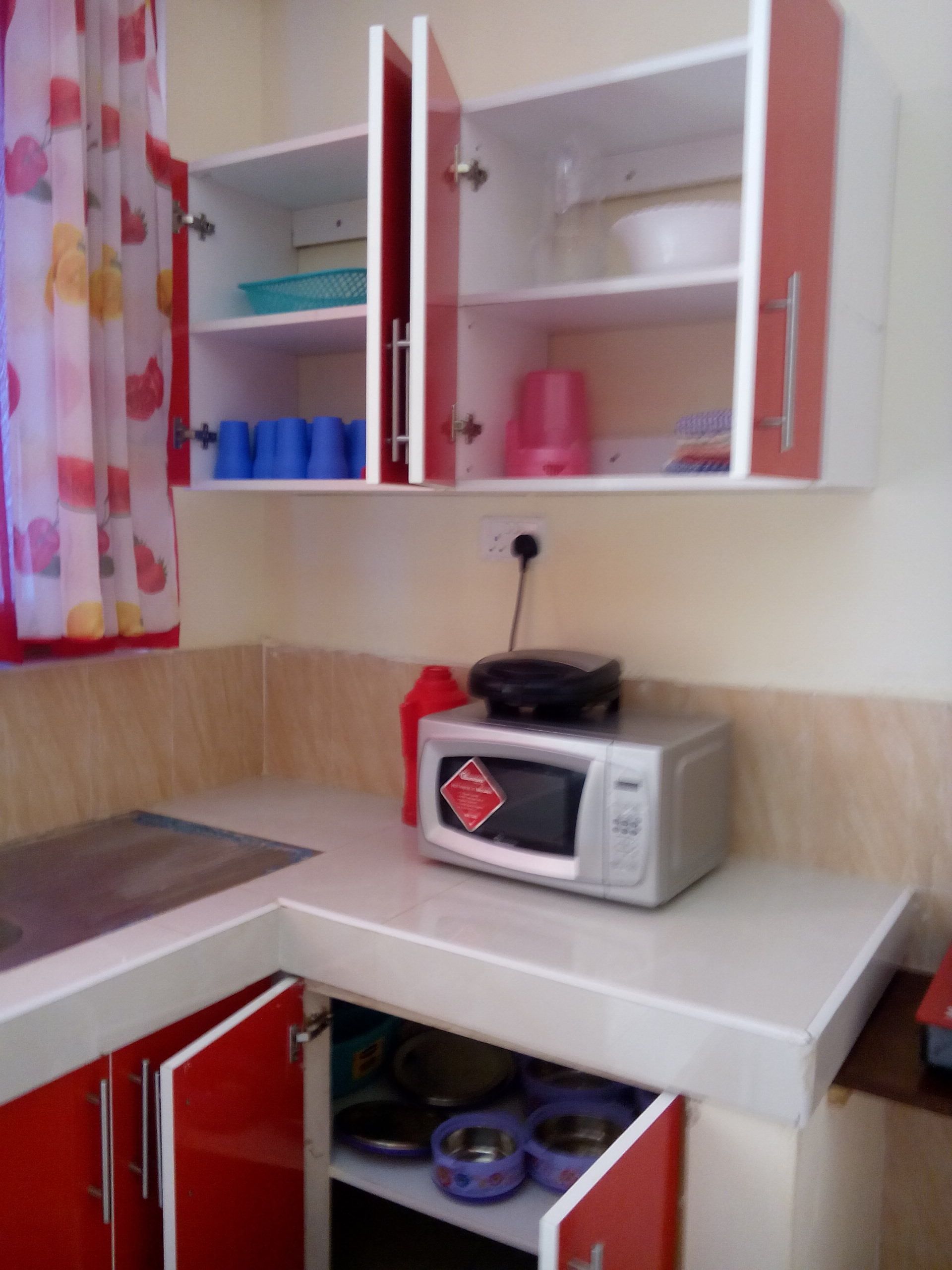 Une petite cuisine équipée d’un four à micro-ondes, d’un meuble rouge et d’une étagère avec des récipients bleus.