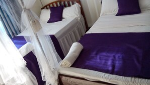 A room with two beds, each with white and purple bedding, and a canopy bed with a white canopy.