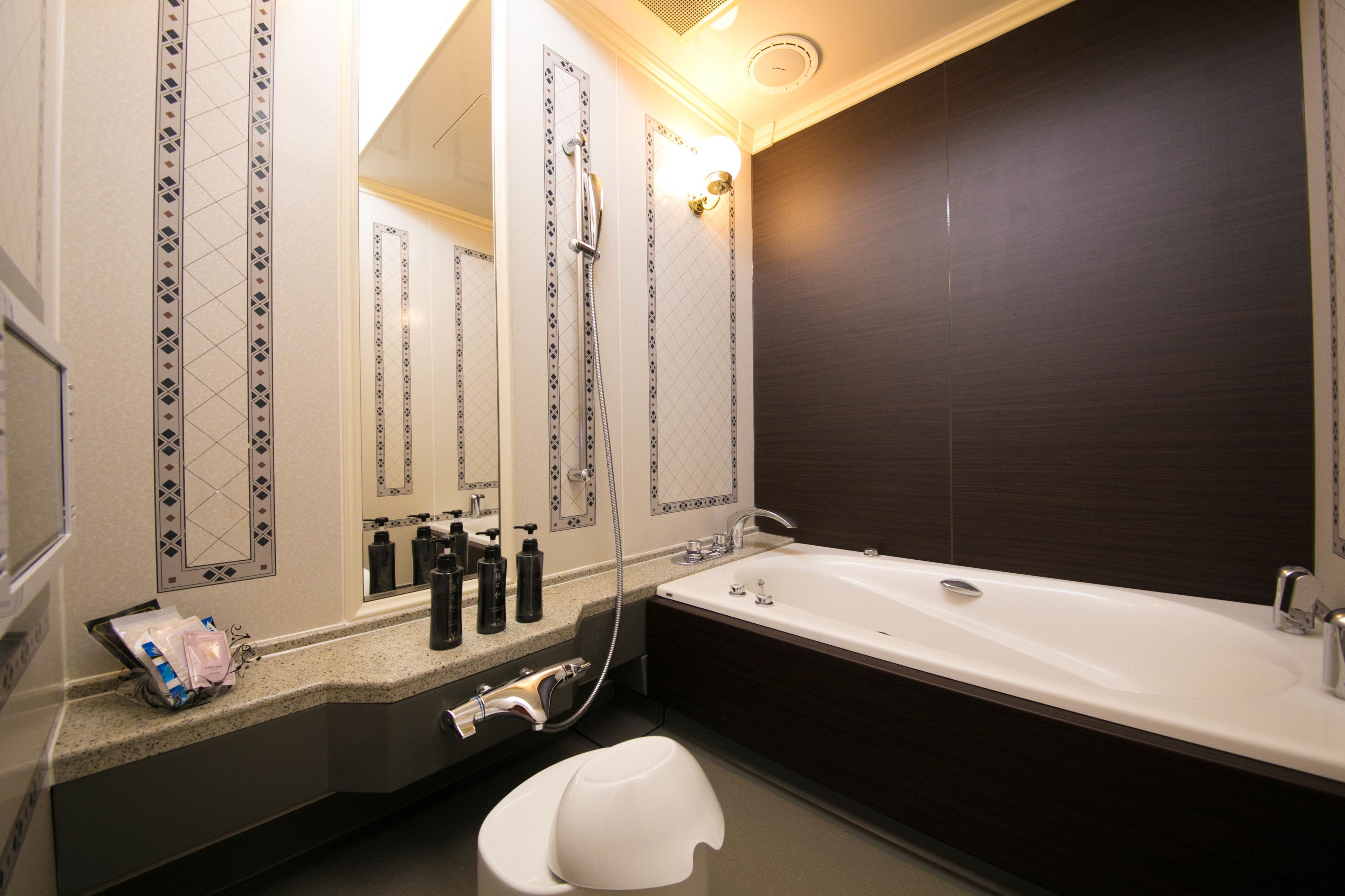 A modern bathroom with a large mirror, a bathtub, and a countertop with toiletries.
