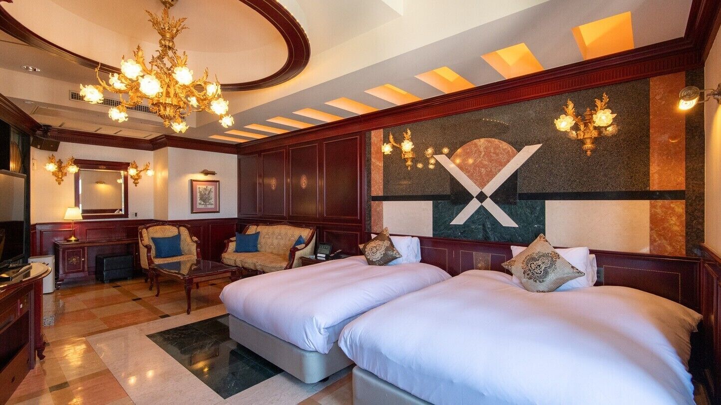 Habitación de hotel con una cama grande, un candelabro, una chimenea y una pared con un gran símbolo 'X'.