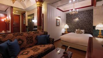A hotel room with a patterned sofa, a bed, a chandelier, and a large mirror.