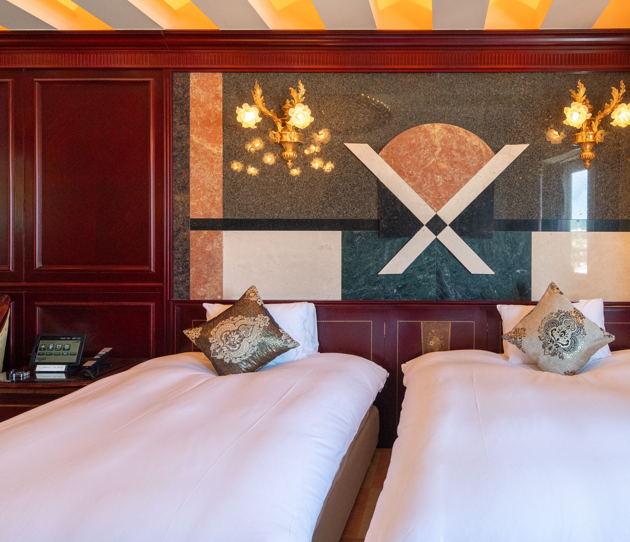 A hotel room with two beds, a large decorative wall, and a desk with a phone.