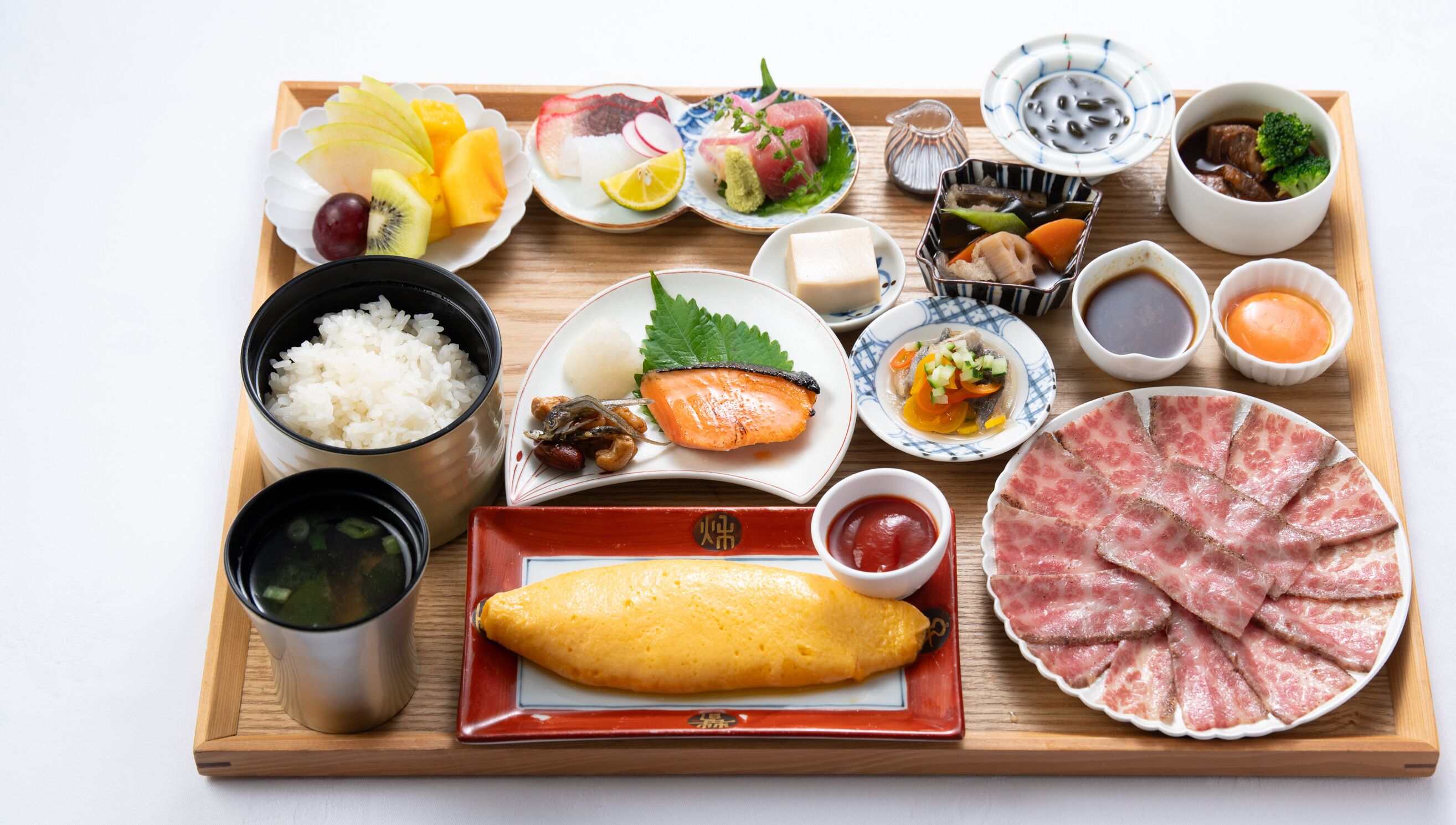 Una bandeja de madera con diversos platos japoneses, incluyendo arroz, sashimi y una variedad de frutas y verduras.