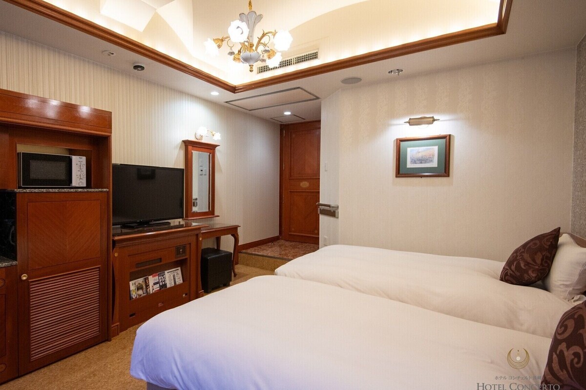 A hotel room with a bed, a TV, a minibar, and a wooden cabinet.