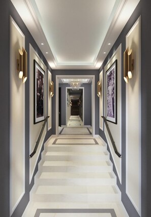 Un couloir avec un escalier, des tableaux encadrés et des appliques murales.