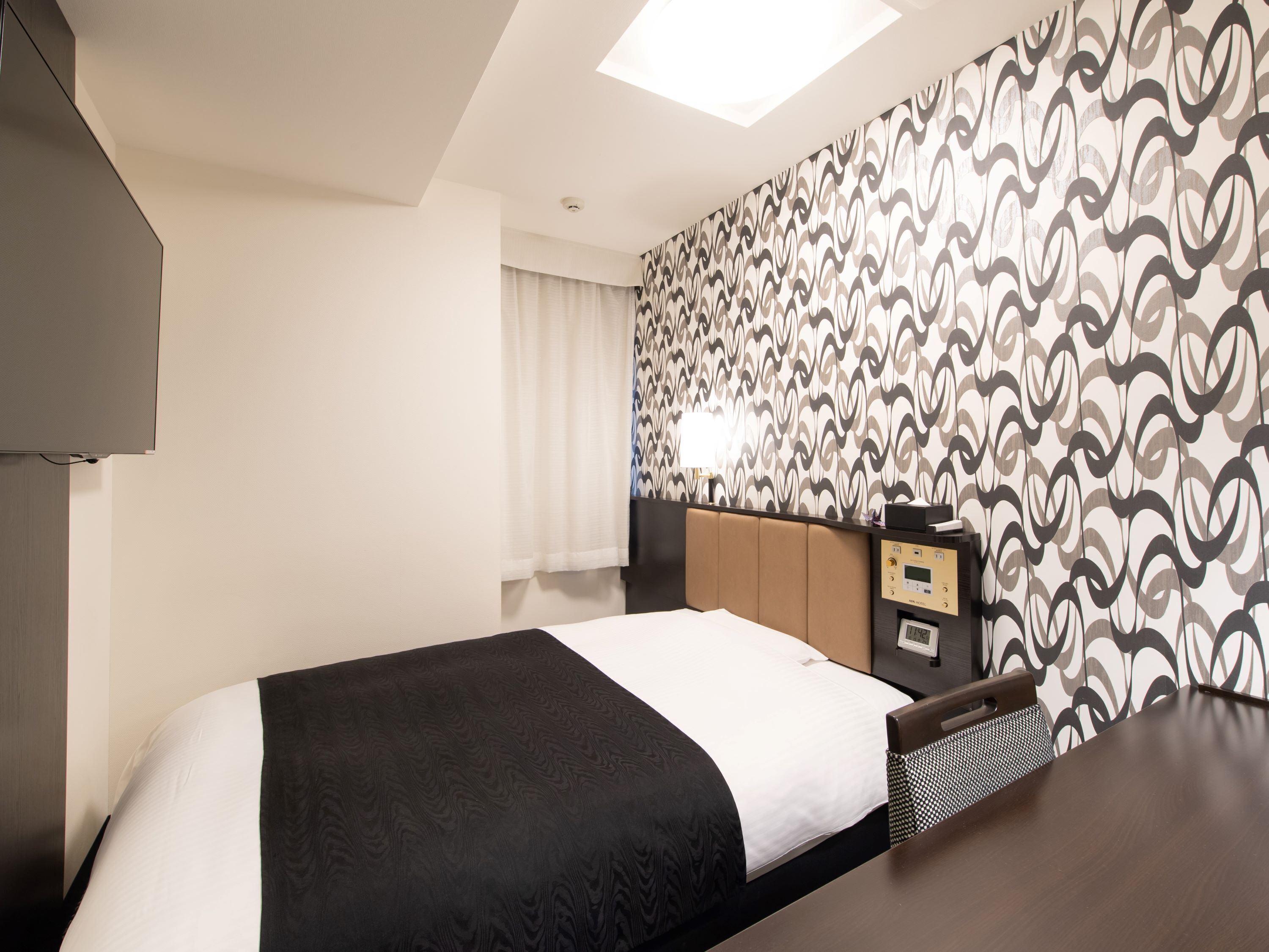 Habitación de hotel con una cama, un escritorio, una lámpara y un papel tapiz estampado.
