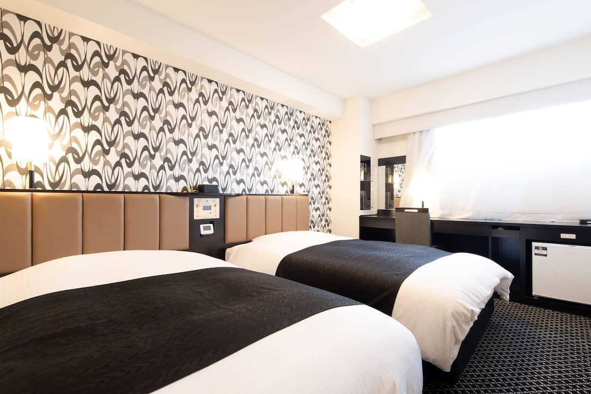 Habitación de hotel con dos camas, un escritorio, una silla, un espejo y un papel tapiz estampado.
