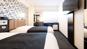Habitación de hotel con dos camas, un escritorio, una silla, un refrigerador pequeño y un televisor.